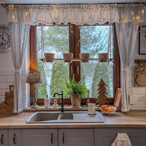 Könnte beinhalten: Eine Küchenspüle mit zwei Becken, grauen Schränken und einer Arbeitsplatte aus Holz. Über der Spüle befindet sich ein Fenster mit weißen Vorhängen und einem Holzregal mit Topfpflanzen. Das Fenster ist mit Lichterketten und einem kleinen Weihnachtsbaum aus Holz dekoriert.