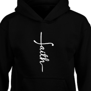 Puede incluir: Sudadera con capucha negra con un gr&aacute;fico blanco de una cruz y la palabra "Fe" escrita verticalmente.