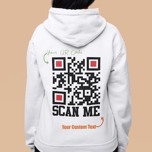 May include: White hoodie with a black and white QR code on the back. The text "Your QR Code" and "SCAN ME" are above and below the code. The text "Your Custom Text" is below the code with an arrow pointing to it.