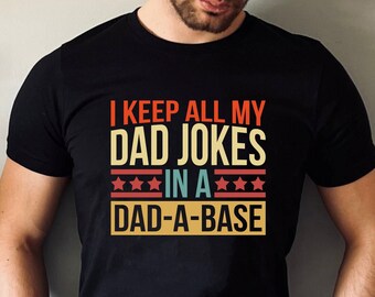 May include: A black t-shirt with a vintage-style graphic that reads "I keep all my dad jokes in a dad-a-base".