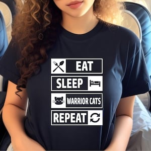 Könnte beinhalten: Ein schwarzes T-Shirt mit weißem Text, der "Essen, Schlafen, Kriegerkatzen, Wiederholen" lautet, mit einem Katzenkopf-Symbol und einem Gabel- und Löffel-Symbol.