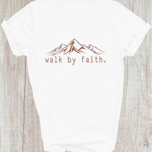 Peut inclure: T-shirt blanc avec un motif de cha&icirc;ne de montagnes brun et le texte "walk by faith."