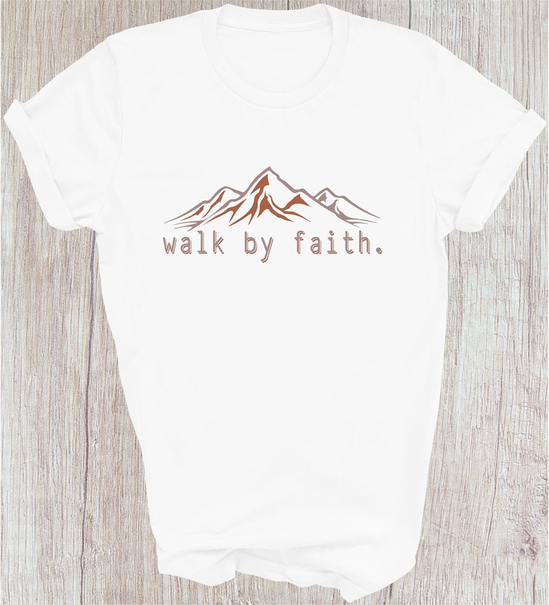 Peut inclure: T-shirt blanc avec un motif de cha&icirc;ne de montagnes brun et le texte "walk by faith."