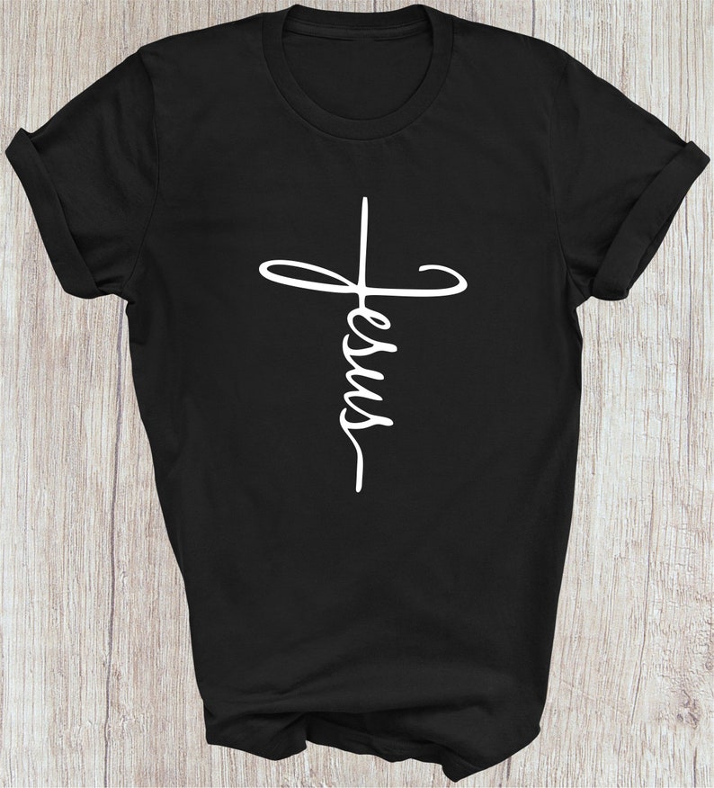 Puede incluir: Camiseta negra con un gr&aacute;fico blanco de una cruz con la palabra "Jes&uacute;s" escrita en su interior.