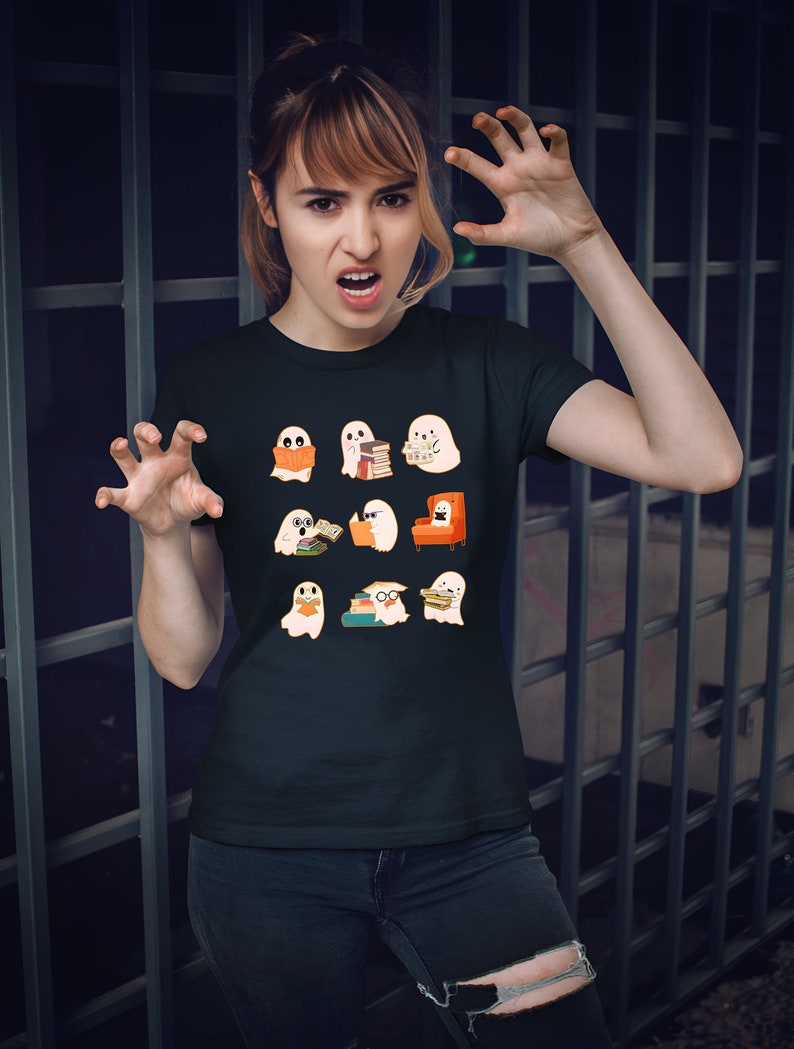 May include: Black t-shirt featuring a pattern of cartoon ghosts reading books. The ghosts are in various poses, some holding books, others sitting in chairs. The design includes orange, white, and black colors.