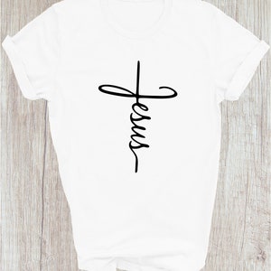Puede incluir: Camiseta blanca con un gr&aacute;fico negro de una cruz con la palabra "Jes&uacute;s" escrita dentro.