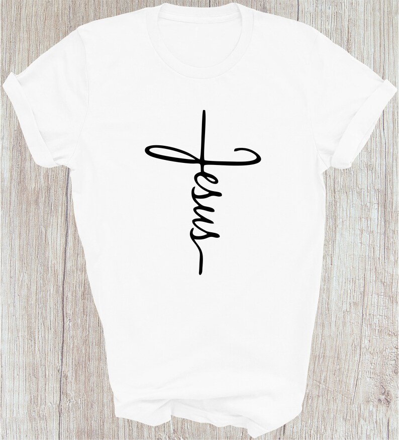Puede incluir: Camiseta blanca con un gr&aacute;fico negro de una cruz con la palabra "Jes&uacute;s" escrita dentro.