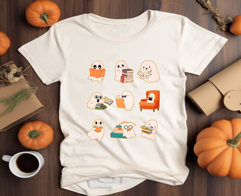 May include: Cream-colored t-shirt featuring a collection of cartoon ghosts reading books. The ghosts are in various poses, some with glasses, and one is seated in an orange armchair. The design has a Halloween or fall theme.