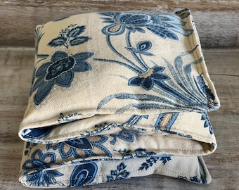 Könnte beinhalten: Ein gefaltetes, cremefarbenes Stoffquadrat mit einem blauen Blumenmuster. Der Stoff ist weich und hat einen dezenten Glanz. Das Quadrat ist in der Hälfte gefaltet und dann noch einmal in der Hälfte, wodurch eine kompakte Form entsteht.