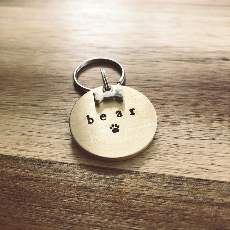 May include: Gold dog tag with a bone charm and the word "bear" engraved on it. A paw print is also engraved on the tag.
