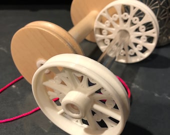 May include: A white wooden yarn swift with two spools and a red string. The swift has a decorative design on the wheels.