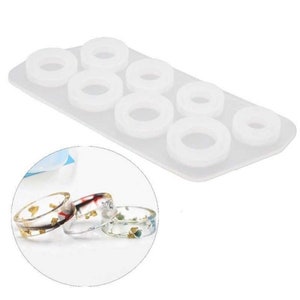 May include: White silicone mold with six round ring shapes. The mold is used to create resin rings. Four finished resin rings with different colors and designs are shown.