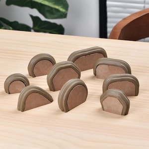 May include: A collection of nine small, semi-circular and rectangular brown silicone edge protectors with flat, light brown adhesive backing surfaces. These protective guards feature a smooth, rounded outer rim and a flat base for mounting.