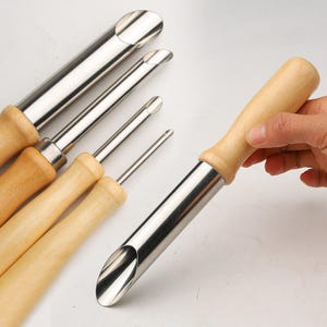May include: Set of five stainless steel cookie cutters with wooden handles. The cutters are different sizes and shapes, including round, oval, and heart shapes.