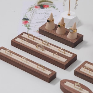 Peut inclure: Un ensemble de présentoirs à bagues en bois avec un revêtement en velours. Les présentoirs sont disponibles en différentes formes et tailles, notamment un présentoir conique à trois fentes et un présentoir rectangulaire à plusieurs rangées.