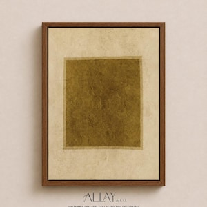 May include: A framed wall art piece featuring a central dark olive green square set against a textured, off-white background. The artwork is enclosed in a medium-toned wooden frame. The text ALLAY & CO. FOR HOMES THAT FEEL COLLECTED, NOT DECORATED appears below.