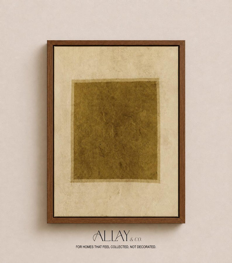 May include: A framed wall art piece featuring a central dark olive green square set against a textured, off-white background. The artwork is enclosed in a medium-toned wooden frame. The text ALLAY & CO. FOR HOMES THAT FEEL COLLECTED, NOT DECORATED appears below.