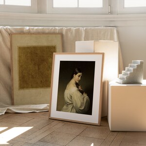 May include: A framed art print featuring a portrait of a person with dark hair in a light-colored garment, positioned next to a second framed print with a solid mustard-yellow square and a small gray stone staircase sculpture on a white block.