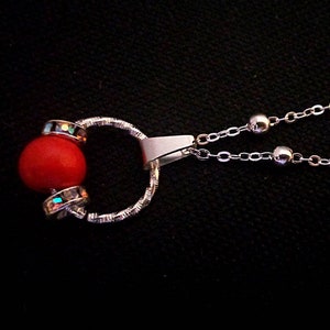 May include: A silver necklace with a red bead and crystal accents. The necklace has a delicate chain and a simple clasp.