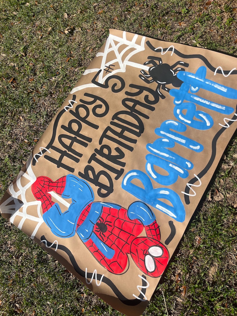 Puede incluir: Una pancarta de cumplea&ntilde;os de papel marr&oacute;n con una ilustraci&oacute;n de Spider-Man. La pancarta dice "Happy 5th Birthday Barrett" en letras negras y azules, con telara&ntilde;as blancas y un dise&ntilde;o de ara&ntilde;a negra.