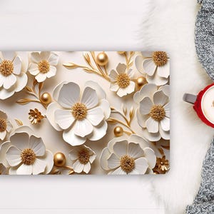 May include: A rectangular laptop skin featuring a cream background with white flowers, golden stems, and small golden spheres. The flowers have layered petals and textured centers. A red mug with a heart-shaped foam design sits on a gray knit fabric.