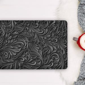 May include: A rectangular laptop skin featuring a dark charcoal gray surface with a raised, three-dimensional embossed pattern of swirling acanthus leaves, intricate scrolls, and small circular beads covering the entire top surface.