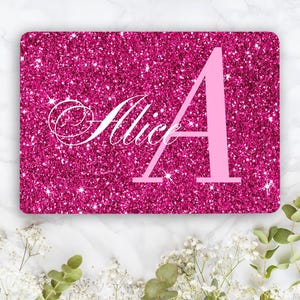 May include: A rectangular sign with a vibrant hot pink glitter texture. The name Alice is written in a white cursive script font, followed by a large, solid light pink capital letter A. The sign has rounded corners and a glossy finish.