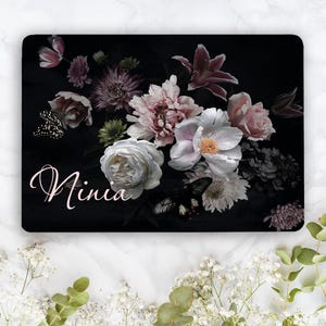 May include: A rectangular plaque featuring a dark black background with a floral arrangement of white, pink, and purple flowers. Two black and white butterflies are positioned among the blooms. The name Ninia is written in white script.