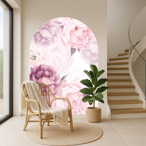 May include: A light-filled interior space featuring a rattan chair with a cream-colored throw, a potted plant, and a large floral mural in shades of pink and purple. A round jute rug sits beneath the chair and plant, with a staircase visible in the background.