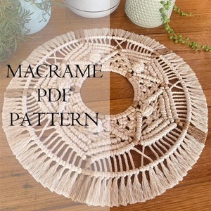 May include: Cream-coloured macrame PDF pattern with a circular design and fringe. The text "MACRAME PDF PATTERN" is displayed on the macrame. The macrame is on a wooden surface, with potted plants in the background.