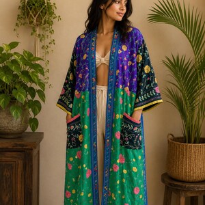 May include: A long, open-front kimono-style robe featuring a vibrant color-blocked design. The upper section is deep purple, while the lower portion is bright green. It is adorned with intricate floral embroidery, wide sleeves, and two pockets.