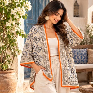 Könnte beinhalten: Eine beige, vorne offene Kimono-Jacke mit blauem geometrischem und floralem Muster, akzentuiert durch leuchtend orangefarbene Säume an den Kanten und am Kragen. Das Kleidungsstück ist mit silberfarbenen Spiegelapplikationen versehen.