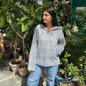 以下が含まれることがあります： Vネックと長袖の青と白の模様のフード付きスウェットシャツ。スウェットシャツは、円と線で構成された幾何学的なデザインです。