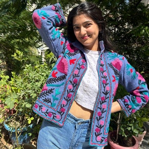 May include: A blue embroidered jacket with floral patterns in pink, red, green, and black. The jacket has a stand-up collar and long sleeves.