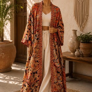 May include: A long, open-front kimono featuring a vibrant, multi-colored paisley pattern in shades of orange, black, and teal. The garment has wide, loose sleeves and a contrasting border along the front opening, worn over a white ribbed crop top.