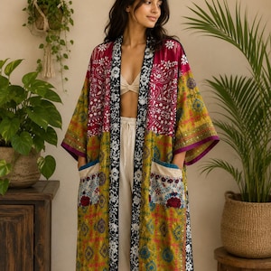 Puede incluir: Un kimono largo abierto por delante con un diseño de patchwork en tonos magenta, verde oliva y amarillo mostaza. La prenda incluye un borde con estampado floral en blanco y negro a lo largo de los bordes delanteros y dos bolsillos grandes.