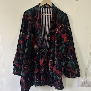 Może przedstawiać: Czarny aksamitny kimono z kwiatowym nadrukiem przedstawiającym czerwone, różowe i zielone kwiaty oraz ptaki. Kimono ma podszewkę w paski.