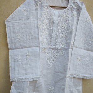 May include: White cotton tunic top with intricate white embroidery featuring floral designs. The top has a round neckline and long sleeves.