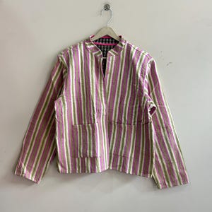 May include: A pink, green, and white striped jacket with a mandarin collar and two front pockets. The jacket is hanging on a wooden hanger against a white wall. The interior lining is a black and green plaid.