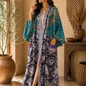 Op de afbeelding: Een lange kimono met open voorzijde en een tweekleurig ontwerp. Het bovenste gedeelte heeft een blauwgroen en groen paisley-patroon, terwijl het onderste gedeelte een donkerblauwe basis heeft met een meerkleurige paisley-print en twee zakken.