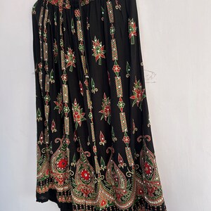 May include: A black maxi skirt with a colorful floral print and embellishments. The skirt has an elastic waistband and a flowing silhouette.