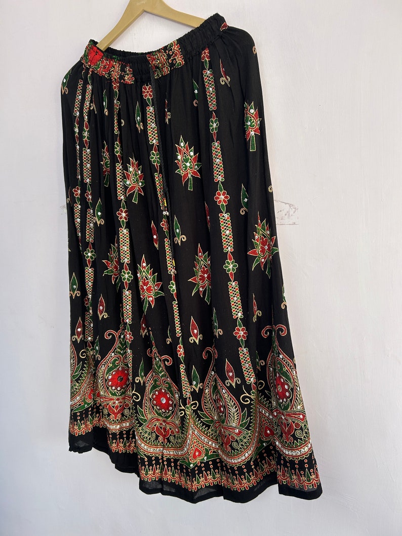 May include: A black maxi skirt with a colorful floral print and embellishments. The skirt has an elastic waistband and a flowing silhouette.