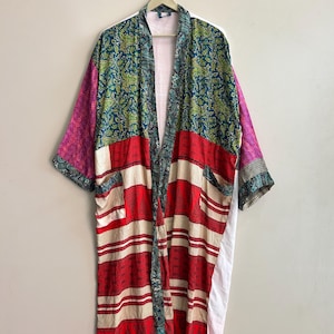 Può includere: Una vestaglia lunga aperta sul davanti con un design patchwork caratterizzato da vari motivi e colori, tra cui rosso scuro, verde acqua, verde e magenta. Il capo presenta maniche larghe, un collo a scialle e due tasche frontali.
