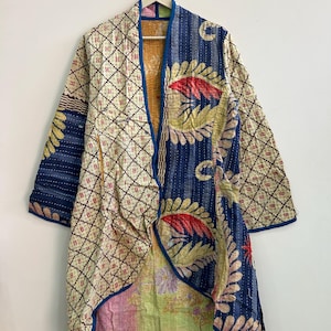 May include: A long-sleeved jacket made from quilted fabric featuring a mix of patterns. One side displays a cream background with a dark brown grid, while the other side features large blue, red, and yellow leaf motifs. The hem reveals a light green and pink floral lining.