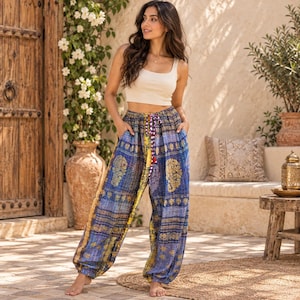 May include: A beige sleeveless crop top paired with loose-fitting, high-waisted harem trousers. The trousers feature a vibrant blue and yellow patterned fabric with intricate gold-toned paisley motifs, a gathered elastic waistband, and a drawstring tie.