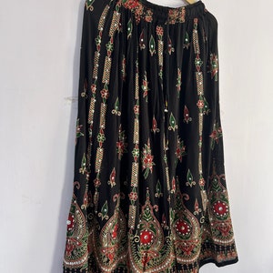 May include: A black maxi skirt with a floral print and gold and silver embellishments. The skirt has a drawstring waist and a flowing silhouette.