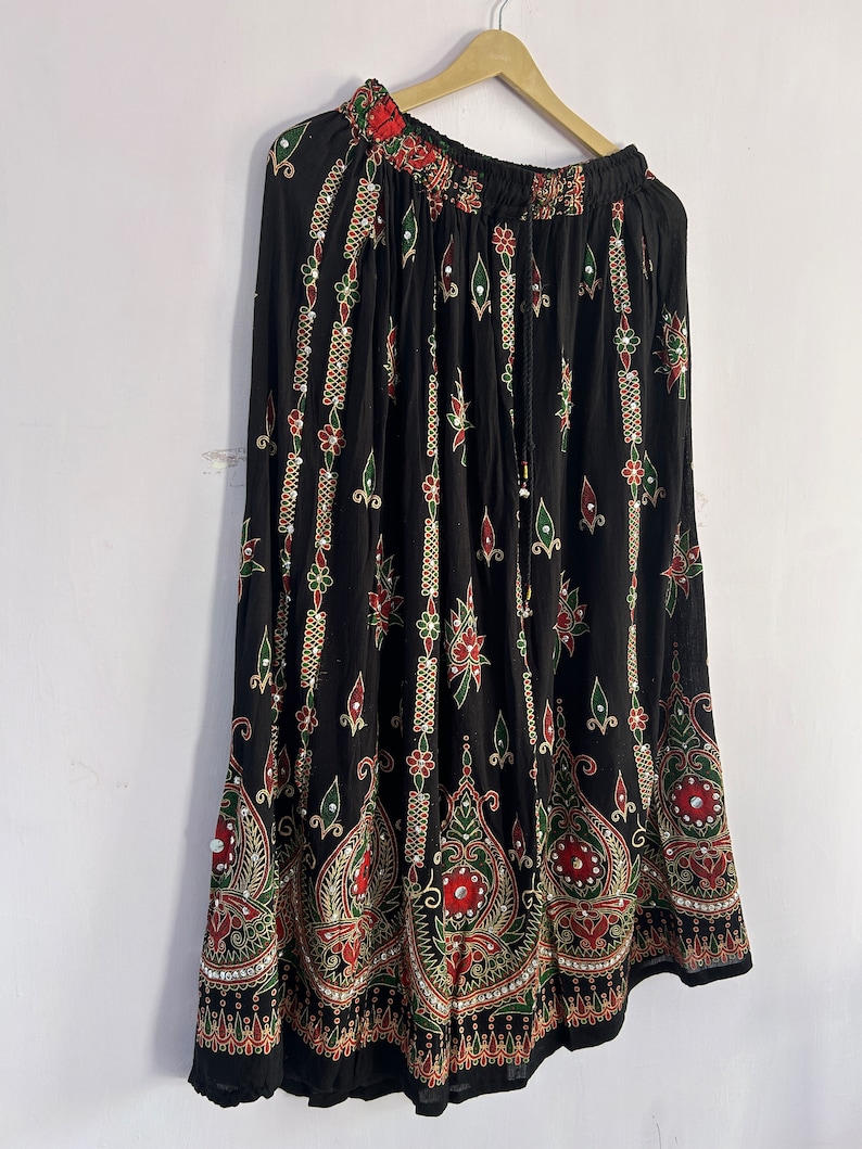 May include: A black maxi skirt with a floral print and gold and silver embellishments. The skirt has a drawstring waist and a flowing silhouette.