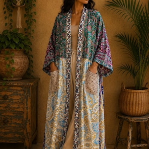 Könnte beinhalten: Ein langer Kimono mit offener Vorderseite, der ein lebendiges Patchwork aus Paisley-Mustern in Grün-, Blau-, Gelb- und Violetttönen aufweist. Das Kleidungsstück verfügt über einen kontrastierenden Blumenbesatz an den Vorderkanten und zwei große Taschen.