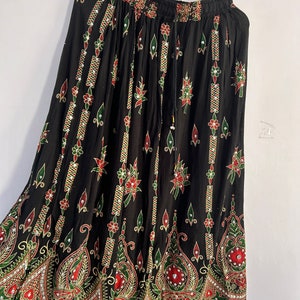 May include: A black maxi skirt with a colorful floral print and embellishments. The skirt has an elastic waistband and a drawstring.