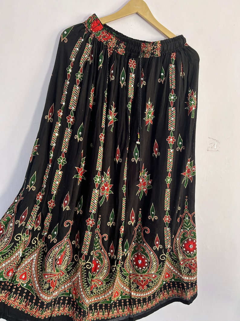 May include: A black maxi skirt with a colorful floral print and embellishments. The skirt has an elastic waistband and a drawstring.